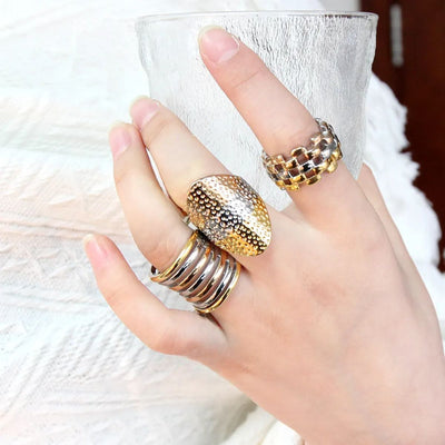Model holding a glass wearing modern industrial style tri-colour rings. Chunky statement rings that draw the eye.