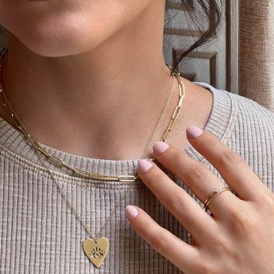 Model showcasing our Women's Gold Necklaces - Australia collection. Includes a 45cm 14kt yellow gold chain with heart-shaped pendant featuring an evil eye, and a 40cm 2.6mm paperclip chain in 14kt yellow gold.