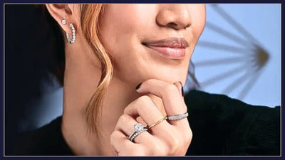 Model with hair draped down her face and a black t-shirt wearing a pair of diamond stud earrings, diamond hoops as well as four diamond rings, including a halo diamond engagement ring. Shop now at Jewels of St Leon