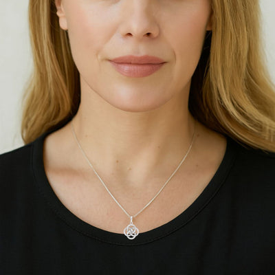 Professional woman with sandy blonde hair and emerald green eyes wearing a sterling silver Celtic knot diamond pendant on a fine 1mm cable chain. The necklace rests gracefully at her collarbone against a black top.