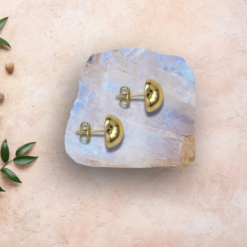 The 10mm Half-Domed Stud Earrings in 9ct Yellow Gold are elegantly showcased on a colourful rock against a sandstone background, emphasizing their luxurious and versatile style.