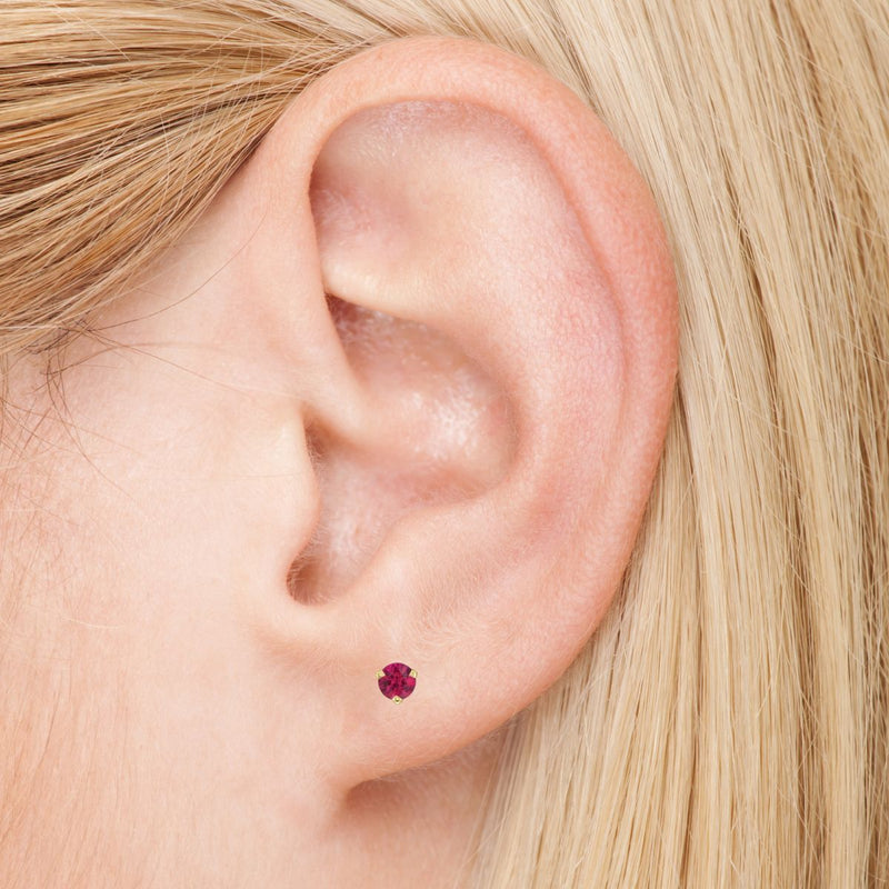 In this elegant photo, a model gracefully wears a 3.0mm natural ruby earring in her left ear, exuding sophistication and refinement. Shop gold stud earrings from Jewels of St Leon.