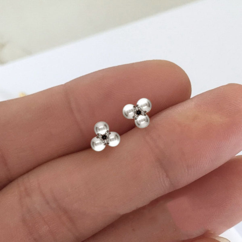 3mm sterling silver three-ball stud earrings shown resting on fingertips for scale. The highly polished spheres reflect light, emphasising their dainty size and minimalist design.