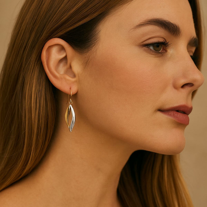 A close-up portrait of a woman wearing 9ct two-tone gold fancy drop earrings, featuring twisted yellow and white gold.