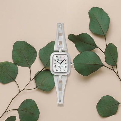 The elegant Amalia Ladies Watch with its shimmering Mother of Pearl dial is artfully displayed against a soft background, surrounded by lush green foliage, highlighting its timeless beauty.