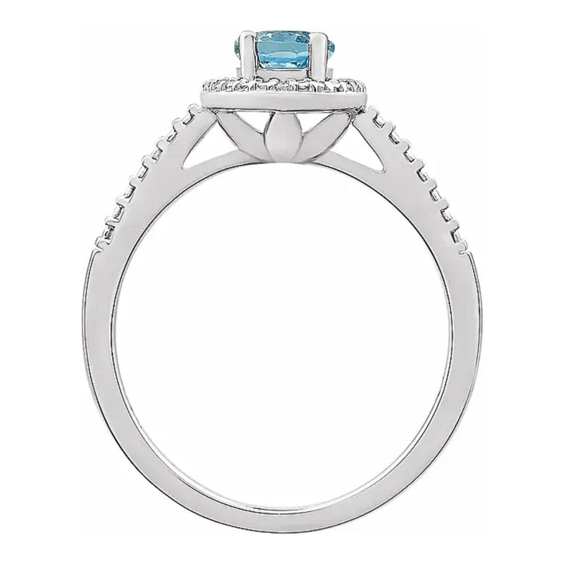 A side view of the Sky Blue 7x5mm Oval Topaz Beaded Halo Ring, emphasising the raised setting of the 7x5mm topaz and the intricate beaded halo design with diamond accents, all crafted in tarnish-resistant rhodium-plated sterling silver. Shop Women&