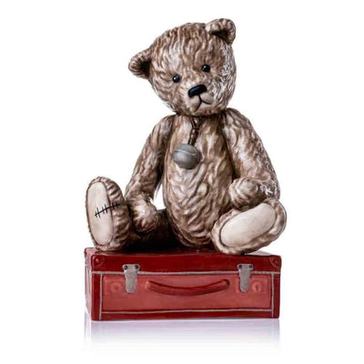 A direct front-facing view of Jake, showcasing his curious expression and delicately hand-painted brown-beige textured fur. The oversized silver bell around his neck and the red suitcase base complete the charming display.