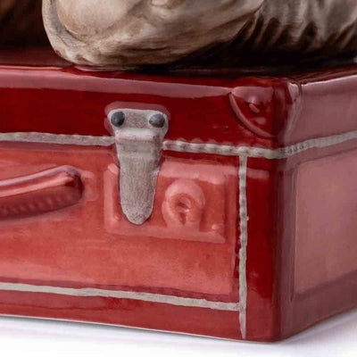 A close-up of the vibrant red suitcase base, showcasing its detailed surface texture and the traditional style that Jake is posed upon. The suitcase complements the bear’s warm tones and adds character to the figurine.