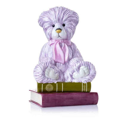 A stunning front-facing shot of the Charlie Bear 2024 figurine, showcasing its delicate hand-painted lilac fur, soft pink satin bow, and charming expression, seated atop two intricately detailed books.