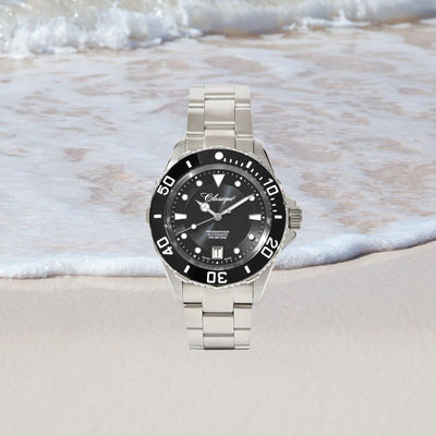 Pro-Mariner Professional Divers Watch with black dial on a sandy beach with waves in the background