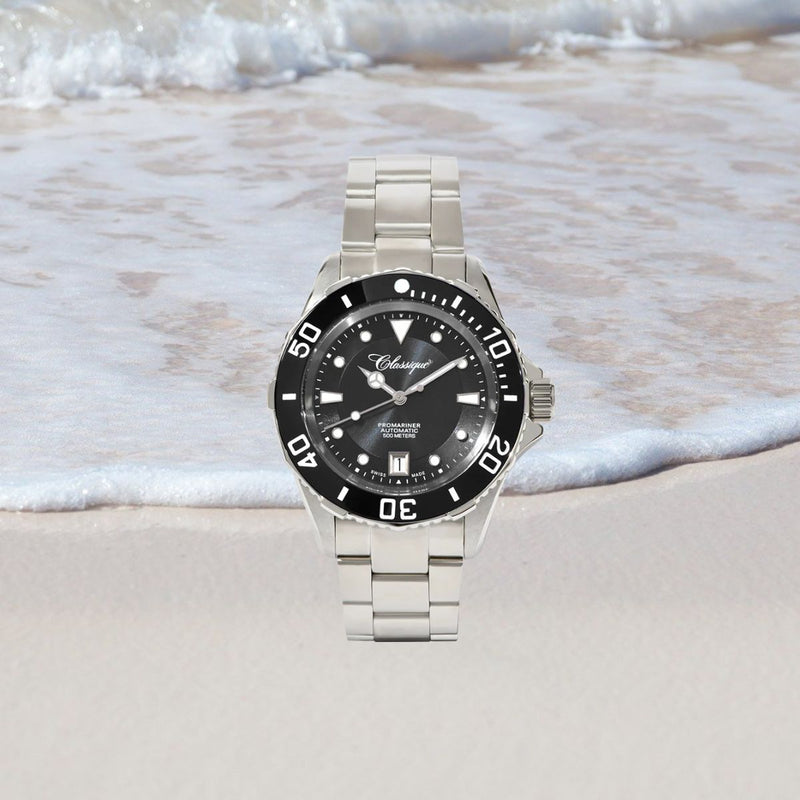 Pro-Mariner Professional Divers Watch with black dial on a sandy beach with waves in the background