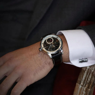 Classique Aviator Skeleton Watch with 47mm open-dial design, Swiss mechanical movement, black leather band, and sapphire crystal face, on a male model wearing a suit.