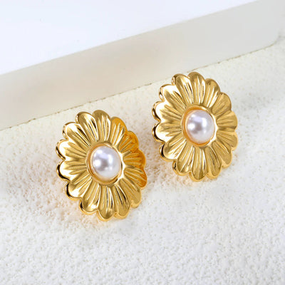 Angled view of the gold daisy pearl studs resting on a textured ivory surface beside a minimalist block.
