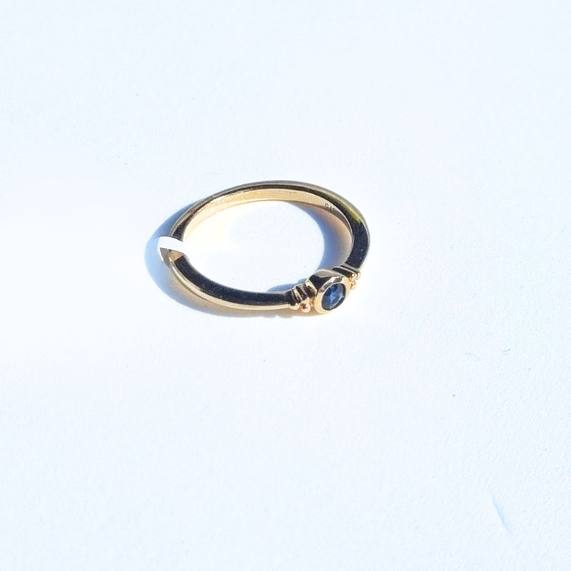 The ELLIN Ring lying flat at a 45° angle to the right, highlighting the sparkling blue sapphire and the graceful curvature of the 9kt yellow gold band, perfect for stacking with other rings. Shop gold jewellery Australia at Jewels of St Leon.