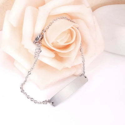 The Stainless Steel Engravable Bracelet draped over a peach rose, showcasing its polished surface and understated elegance, ideal for everyday wear or gifting.