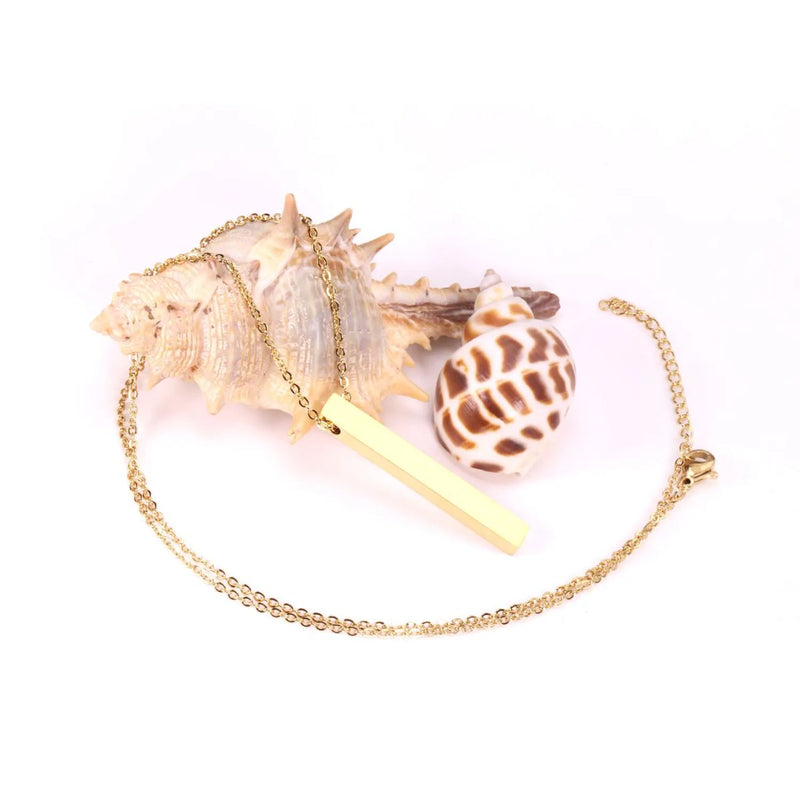 The necklace draped beautifully across a seashell, emphasising its polished gold finish and sophisticated design.