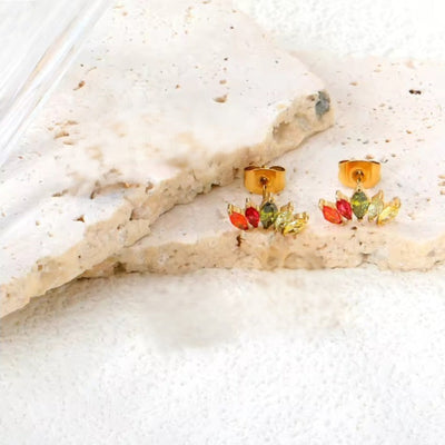 Lifestyle image: rainbow CZ fan studs resting on textured limestone slabs, showing vivid colours against neutral stone.