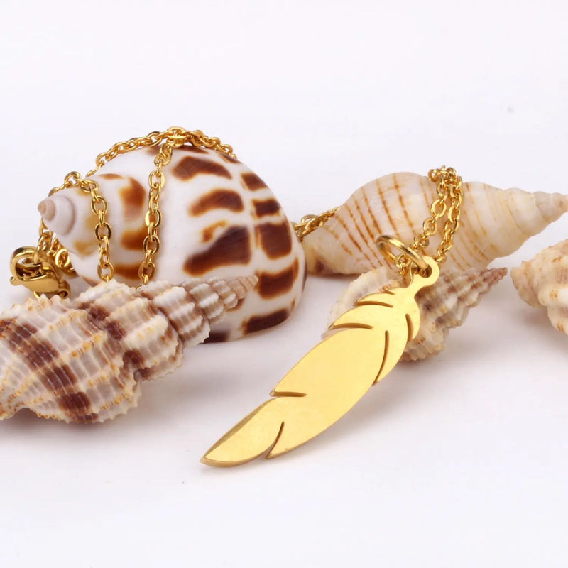 Feather Necklace draped over seashells, highlighting its natural inspiration and soft gold glow against a beachy backdrop.