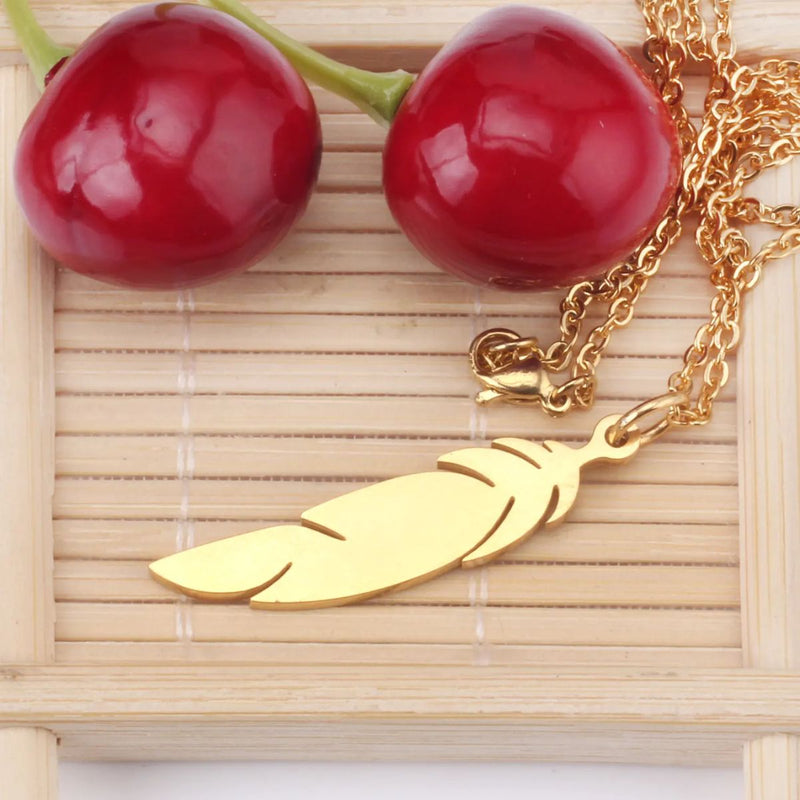 Necklace styled on a wooden tray beside two cherries, showcasing the pendant’s slim shape and golden warmth in a relaxed, earthy setting.