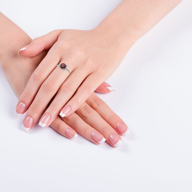 Garnet and diamond silver ring displayed on a models hand. Featuring a 7mm Mozambique Garnet, set with 0.01ctw natural diamonds, this ladies halo-style ring is a beautiful gift for someone special or a treat for yourself, available from Jewels of St Leon.