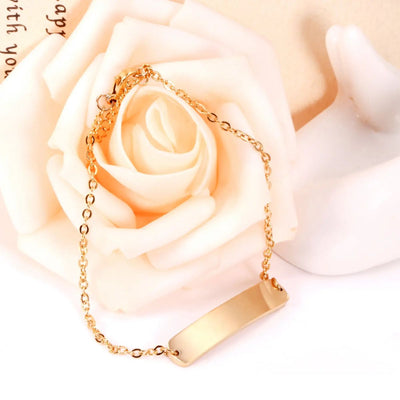 The Gold Engravable Bracelet draped gracefully over a peach rose, capturing its lustrous 18K gold-plated finish and delicate design - ideal for personalisation.