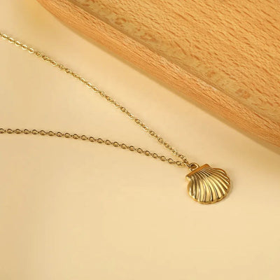 Close-up of the 18K Gold Plated Shell Necklace laying on a soft background next to a wooden board, showcasing its gleaming finish and delicate coastal-inspired pendant.