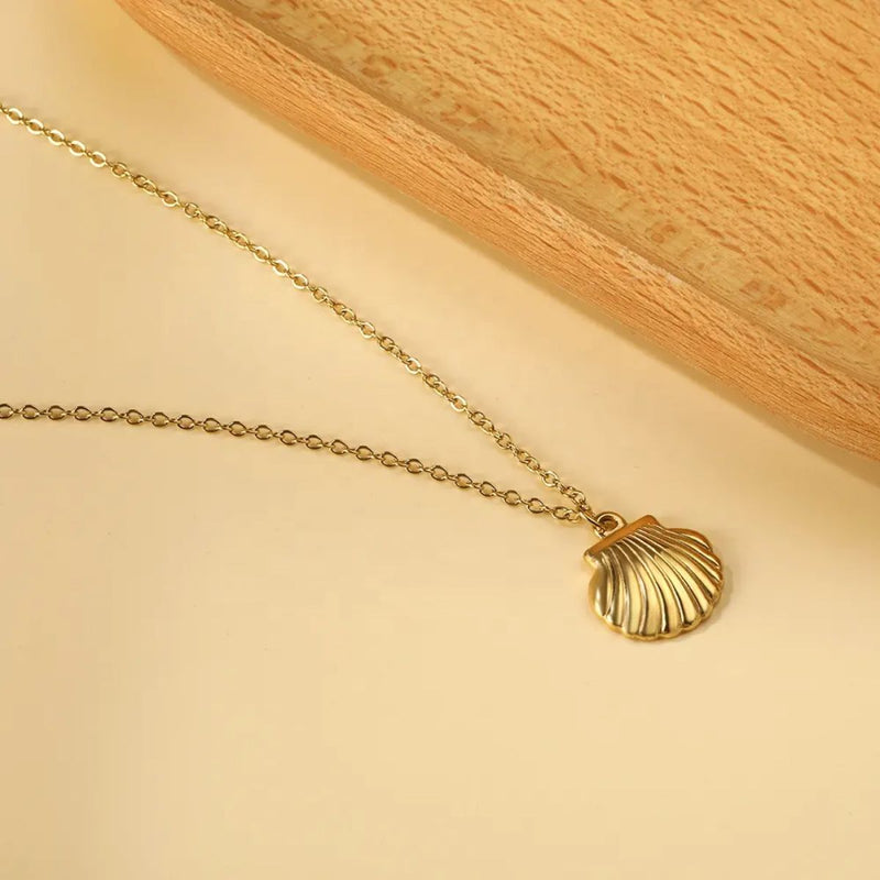 Close-up of the 18K Gold Plated Shell Necklace laying on a soft background next to a wooden board, showcasing its gleaming finish and delicate coastal-inspired pendant.
