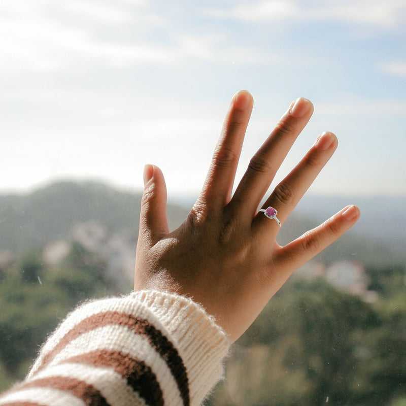 Lab-Created Ruby and Diamond halo-style silver ring on the hand of a model, capturing the sunlight.