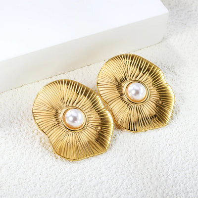 Angled view of ripple-textured lotus pearl earrings resting on a crisp white block, showcasing radiant gold finish and sculptural curves.