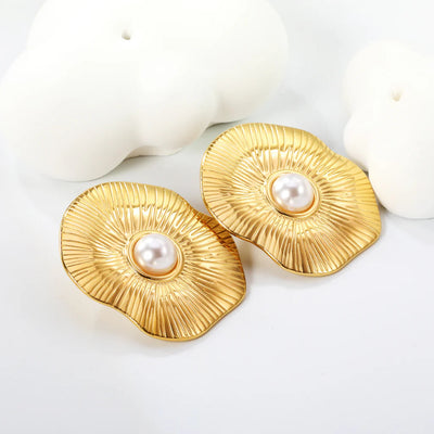 Lifestyle shot of gold lotus pearl studs styled among smooth abstract ceramics on a white backdrop, emphasising organic shape and lustrous centre.