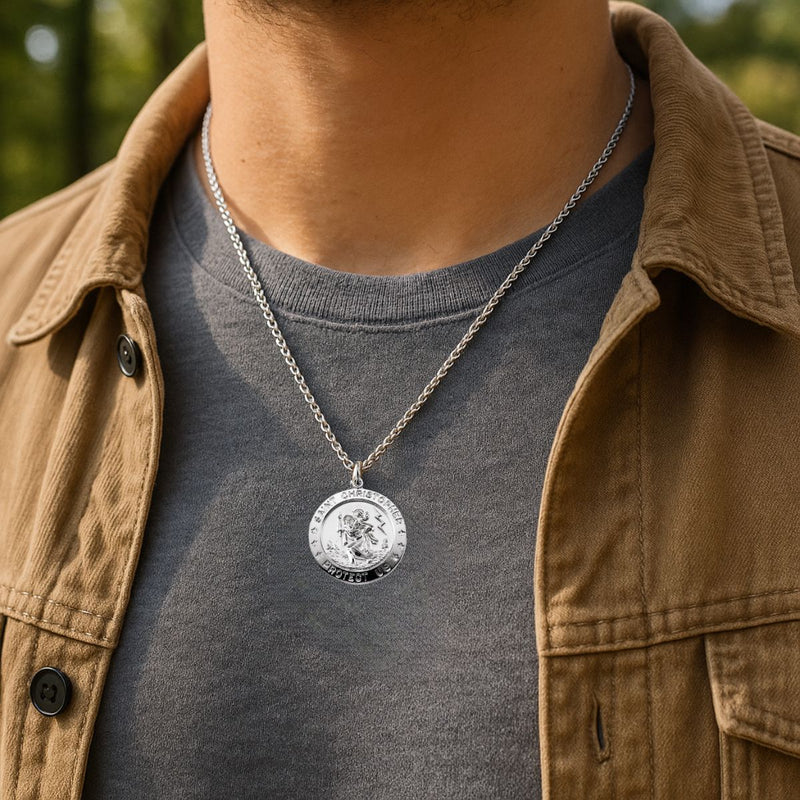 Person wearing a silver necklace with a St Christopher Medal pendant Necklace, wearing a brown jacket and gray shirt.