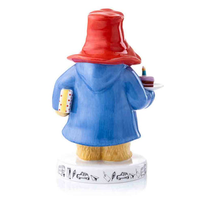 View from the back of Paddington Bear: A Party Colour Figurine - Paddington is featured with his Blue Duffle, iconic red hat and with a piece of cake with a candle and a present under his arm. Set on a beautiful base with iconic London Motifs.