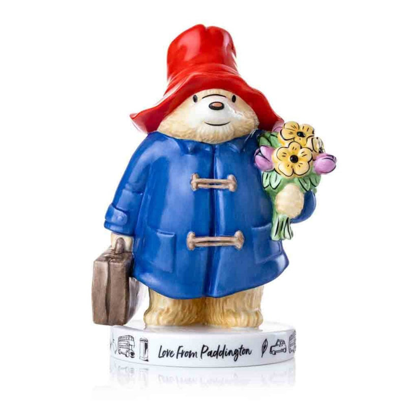 Front View: Paddington Bear, wearing his iconic blue coat and red hat, stands proudly with his brown suitcase in one paw and a bouquet of vibrant flowers in the other. The base reads "Love from Paddington," adorned with iconic London motifs.