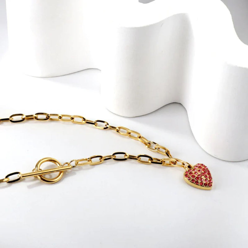The necklace laid on a soft background, showing the warm glow of the gold plating and delicate pink sparkle against the chunky chain.