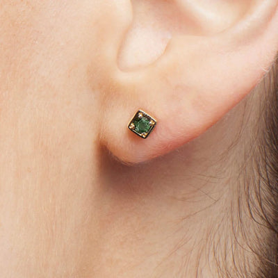 A close-up shot of the Quinn Earrings on a model's ears, showcasing the intricate details of the 3mm green sapphires and the 9kt yellow gold setting. The vibrant green sapphires add a touch of sophistication and elegance. Shop gold earrings for Women from Jewels of St Leon.