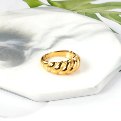 Sitting on a marble coaster is the trendy 18K gold-plated stainless steel croissant ring with a curved design. A statement ring inspired by modern fashion.