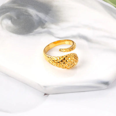 A detailed 18K gold-plated stainless steel snake ring with a tapered design on a marble coaster. A unique wrap-around ring with bold and elegant craftsmanship.
