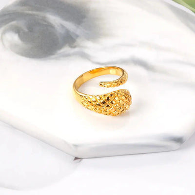 A detailed 18K gold-plated stainless steel snake ring with a tapered design on a marble coaster. A unique wrap-around ring with bold and elegant craftsmanship.