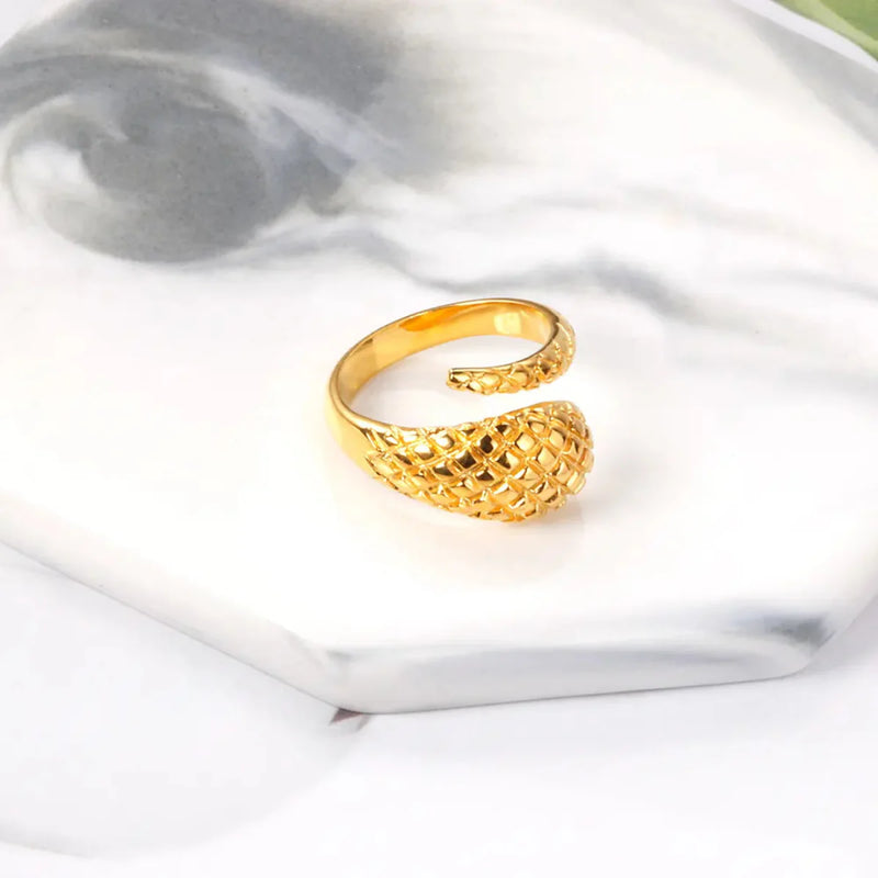A detailed 18K gold-plated stainless steel snake ring with a tapered design on a marble coaster. A unique wrap-around ring with bold and elegant craftsmanship.