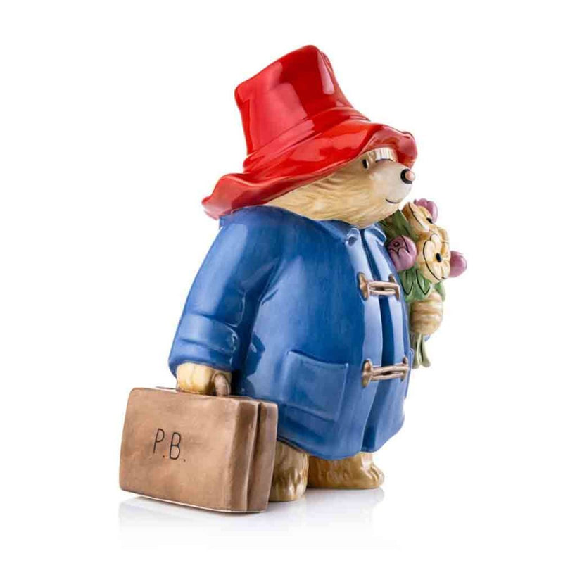 An angled perspective reveals Paddington’s cheerful pose, emphasizing the hand-painted textures of his coat, hat, and the bouquet of flowers he holds lovingly.