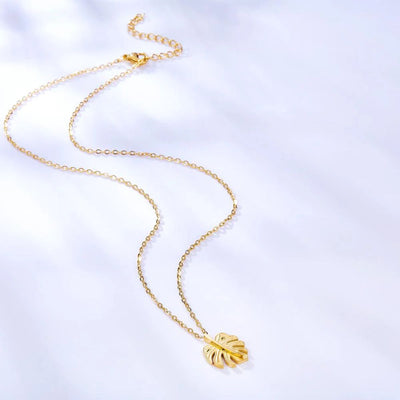 The necklace displayed on a soft blue-grey background, highlighting the warmth of the 18K gold plating and its natural botanical design.