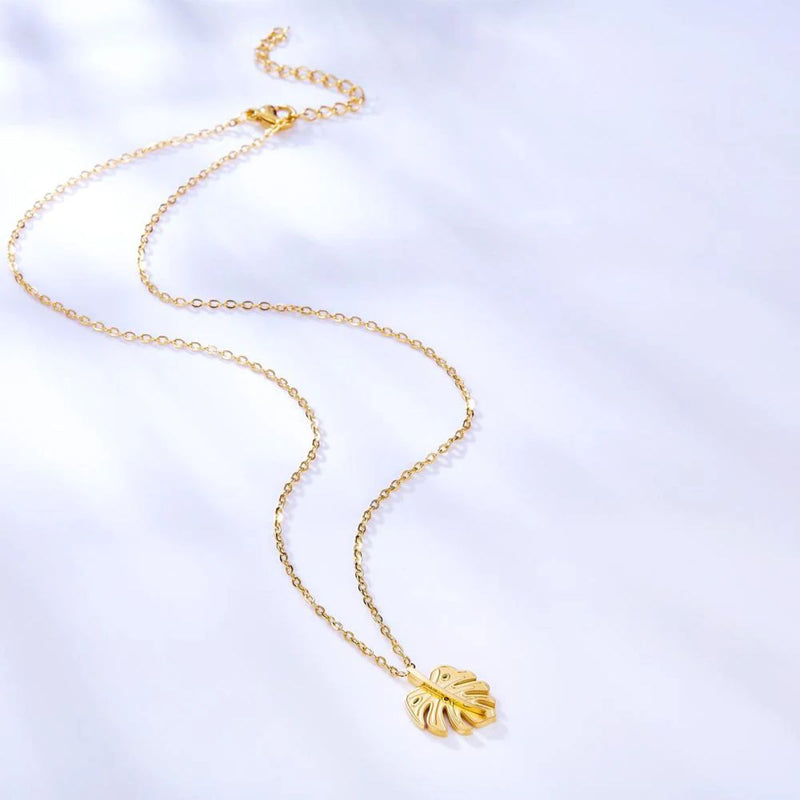 The necklace displayed on a soft blue-grey background, highlighting the warmth of the 18K gold plating and its natural botanical design.