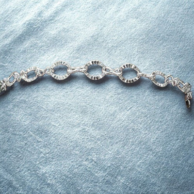 Sterling Silver sparkling oval link bracelet with 5.48mm x 7mm diamond-cut links and figure 8 connectors, shown on a textured blue background.