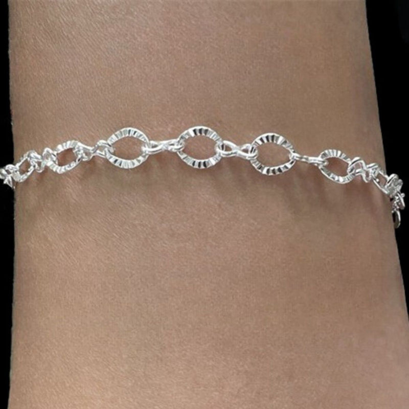 Sterling Silver sparkling oval link bracelet with 5.48mm x 7mm diamond-cut links and figure 8 connectors, shown wrapped around a female wrist in natural light.