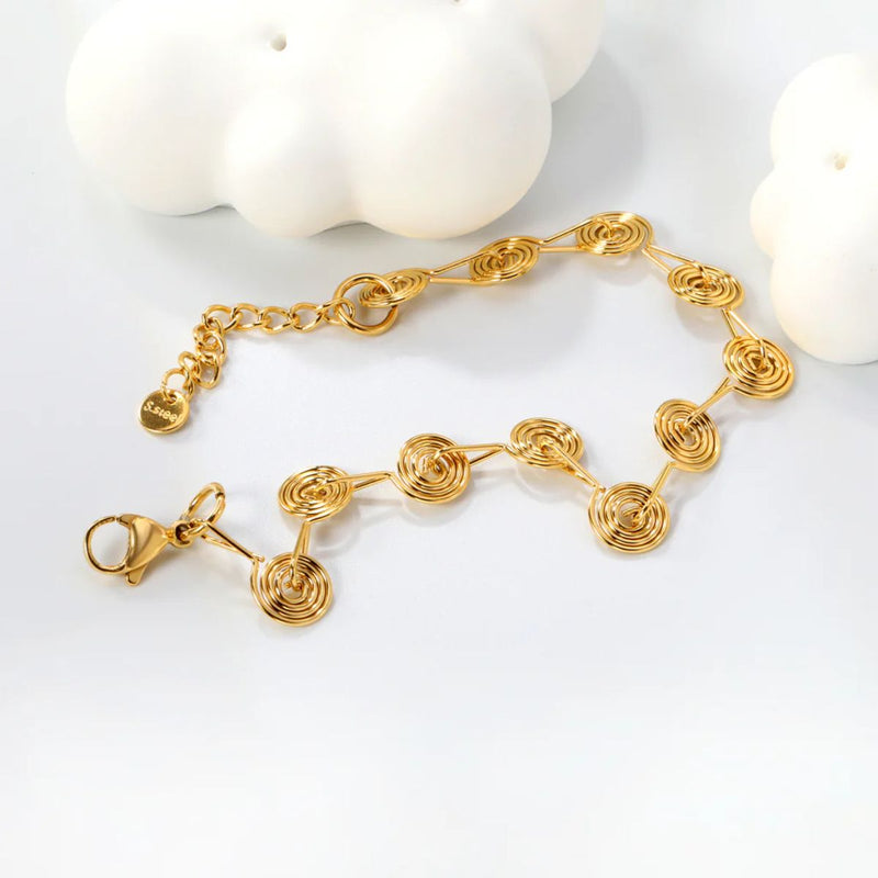 A delicate spiral station charm bracelet in radiant 18K gold-plated stainless steel, symbolising growth and transformation.