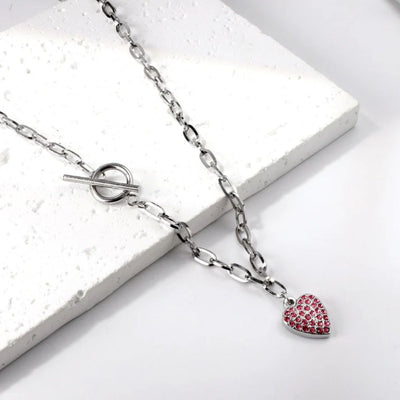 Necklace laid on a sandstone block and soft background, highlighting the vibrant sparkle of pink stones and sleek silver tones of the chunky paperclip chain.