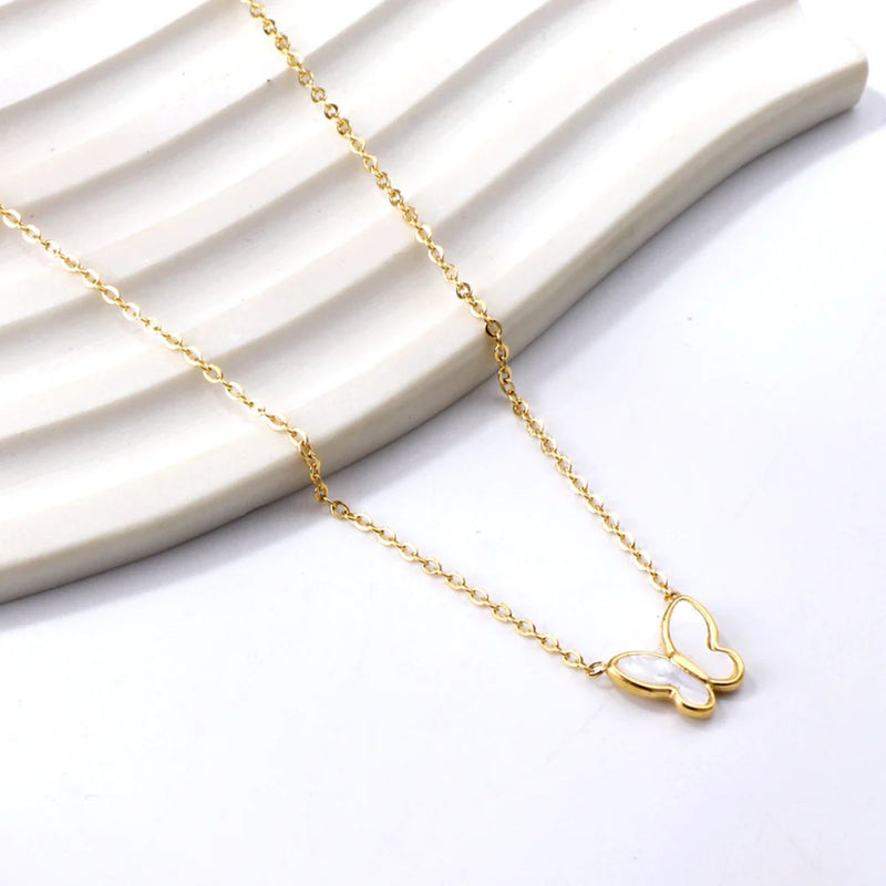 The White Butterfly Necklace elegantly draped down a stepped display, showcasing the clean, minimalist beauty of the white enamel with gold detailing.