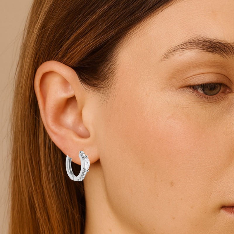 Close-up of a woman wearing silver hoop earrings with oval and round CZ Detail.