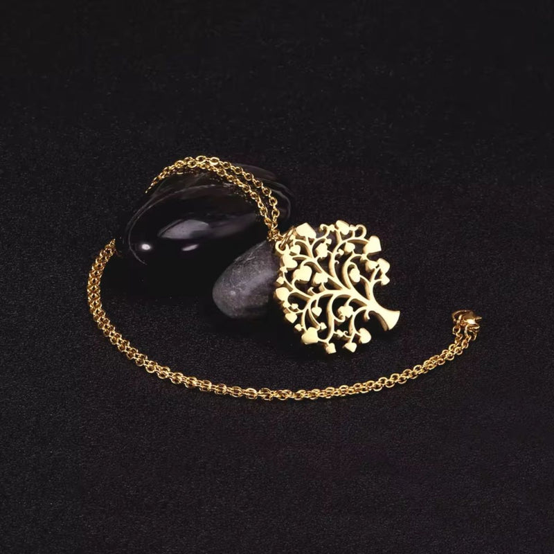 Pendant necklace wrapped around smooth black rocks, with the gold Tree of Life glowing softly against the dark backdrop, symbolising strength and grounding.