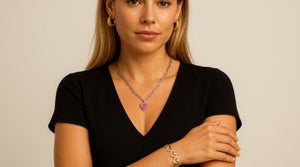 Woman wearing a black V-neck top, and Urban Jewellery pieces including gold hoop earrings, a silver chain with a pink cz heart-shaped pendant and a gold heart bracelet cuff, against a neutral background.